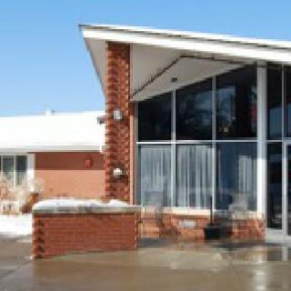 A modern building featuring a brick exterior and large glass windows, with snow on the ground under a clear blue sky.