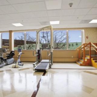 A spacious rehabilitation gym equipped with exercise machines and a staircase, featuring large windows for natural light.