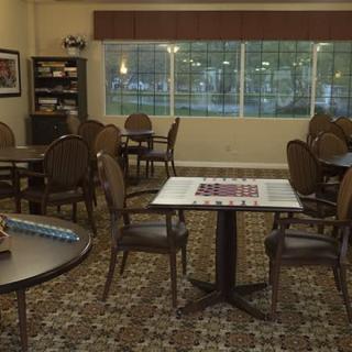 A cozy game room with tables and chairs, featuring a checkerboard and books in the corner.