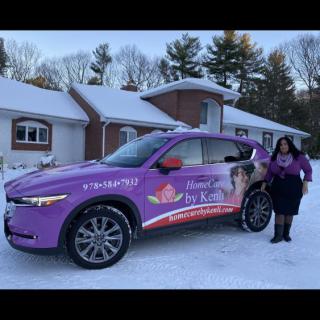 A woman stands next to a purple car with advertising graphics in a snowy outdoor setting.