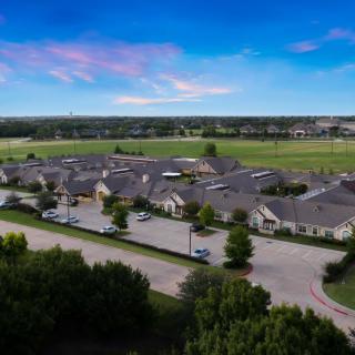 Aerial view of a suburban residential area with rows of houses and surrounding greenery under a blue sky.