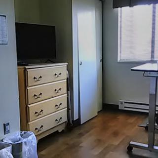 A simple hospital room featuring a television, dresser, and a view out the window.