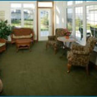 A cozy living room with a seating area, large windows, and a green carpet.