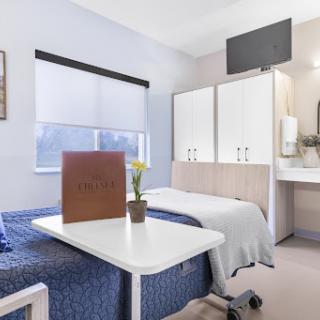 A well-furnished hospital patient room featuring two beds, a small table, and modern amenities.