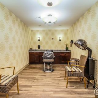 A vintage-themed salon with a barber chair, hair dryer, and waiting area seating.