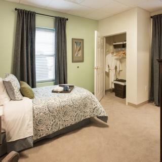 A cozy bedroom with green walls, featuring a bed, curtains, and an open closet.