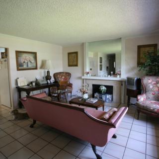 A cozy living room with classic furniture and a fireplace, featuring a pink sofa, armchair, and decorative elements.