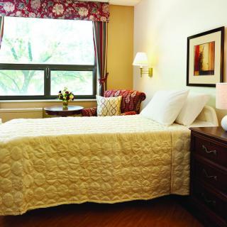 A cozy bedroom with a neatly made bed, a window view, and warm lighting.