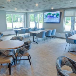 A modern conference room with round tables, comfortable chairs, and a large television.