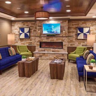 A modern living room with contemporary furnishings, featuring blue sofas, green chairs, a central fireplace, and a mounted television.