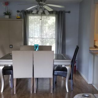 A cozy dining room featuring a table with chairs, curtains framing a window, and a ceiling fan overhead.