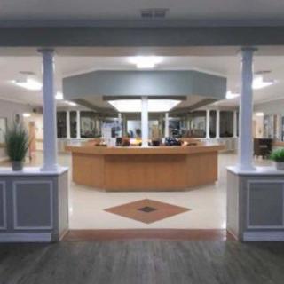A spacious and modern reception area featuring a central wooden desk, surrounded by decorative columns and potted plants.