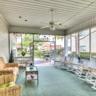A cozy sunroom with wicker furniture and several rocking chairs, featuring large glass windows and a ceiling fan.
