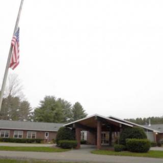 A building with an entrance and an American flag at half-mast, surrounded by trees.