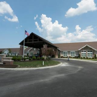 A large building with an entrance drive, surrounded by a well-maintained landscape under a partly cloudy sky.