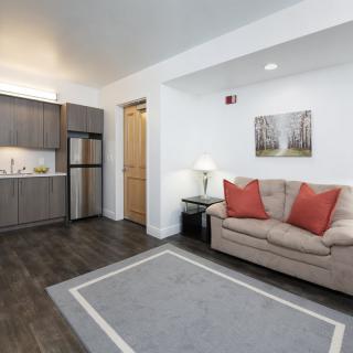 A modern apartment living area featuring a compact kitchen and a cozy sofa with red cushions.