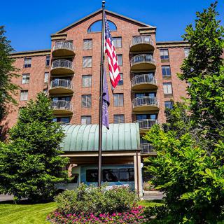 A hotel building with multiple balconies, an American flag in front, surrounded by trees and a clear blue sky.
