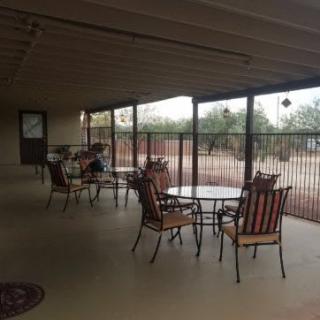 A spacious covered patio with chairs and tables overlooking a backyard.