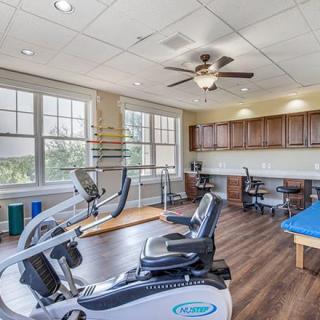 A well-equipped gym room with exercise machines and large windows providing ample natural light.