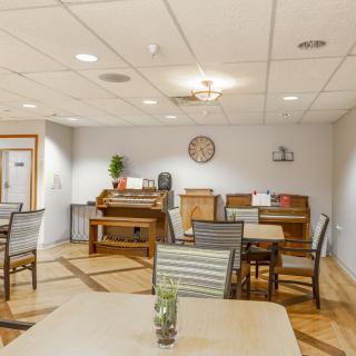 A cozy indoor dining area with tables, chairs, and a piano against the wall.