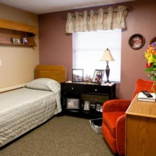 A cozy bedroom with a single bed, an armchair, and a side table decorated with family photos.