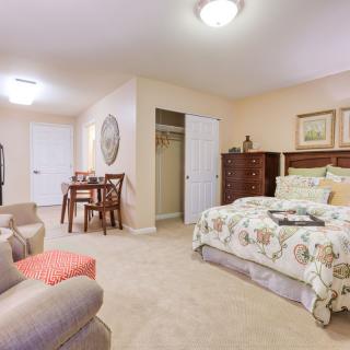 A cozy bedroom with a floral bedspread, wooden furniture, and a small dining area.