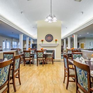 A well-lit dining area with wooden floors, elegantly arranged tables, and chairs.