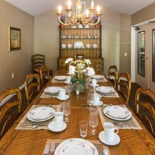 An elegantly set dining room table with fine china and crystal glasses under a chandelier.