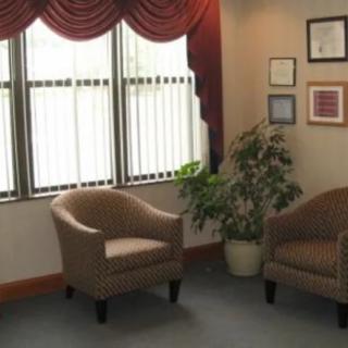 A cozy waiting room with two chairs, potted plant, and large windows.