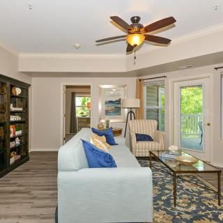 A cozy living room with modern decor, featuring a ceiling fan, sofa, armchair, and a bookshelf.