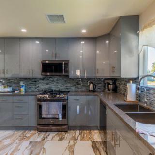 A modern kitchen with gray cabinets, a sleek backsplash, and marble flooring.
