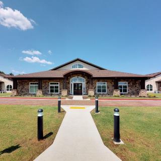 A wide view of a single-story building with a central entrance, surrounded by manicured lawns and under a clear blue sky.