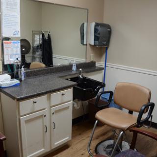 A view of a hair salon space featuring a chair, mirror, and sink.