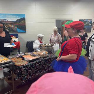 A lively community event featuring attendees in costumes enjoying a buffet of food.