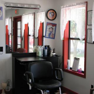 An interior view of a barber shop with a styling station, mirror, and black chair.