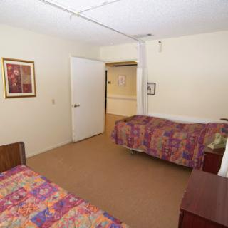 A simple bedroom featuring two beds with colorful bedspreads and a doorway leading to another area.