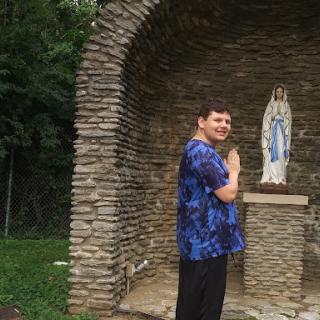 A man praying in front of a religious statue in a serene outdoor setting.