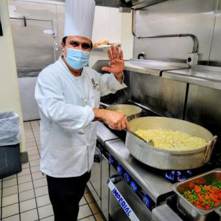 A professional chef cooking pasta in a large pot in a restaurant kitchen.