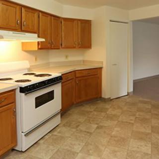 A kitchen interior featuring wooden cabinets, a white stove, and tiled flooring.