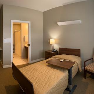 A cozy and simple hotel room featuring a single bed, a bedside lamp, and an accessible bathroom.