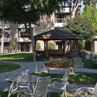 A peaceful garden setting with a gazebo, surrounded by trees and outdoor seating.