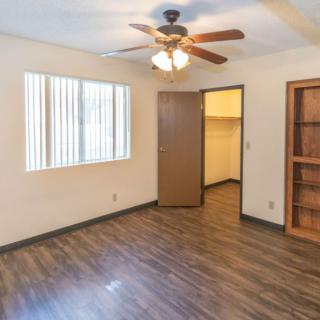 An empty room with a ceiling fan, wooden floor, and built-in shelves.