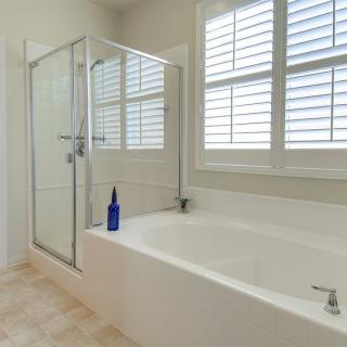 A modern bathroom with a bathtub and glass-enclosed shower next to windows with shutters.