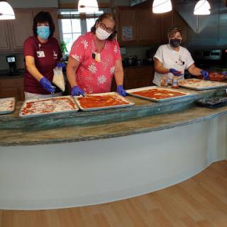 Healthcare workers preparing food in a kitchen setting, demonstrating safety protocols with masks and gloves.