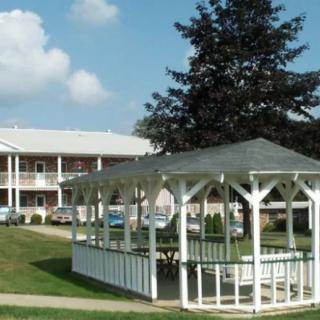 A white gazebo in front of a multi-story building with a lawn and trees.