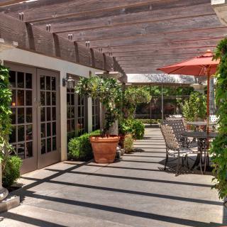 A sunny patio with a pergola, featuring outdoor seating and lush greenery.