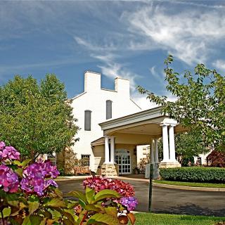 A scenic view of a building entrance surrounded by colorful flowers and trees under a bright blue sky.