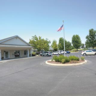 A single-story building with a flagpole, surrounded by a landscaped parking lot and several parked cars.