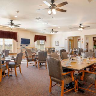 A spacious dining area with neatly arranged tables and chairs, featuring ceiling fans and warm lighting.
