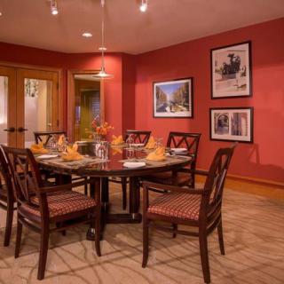 A warmly lit dining room with red walls features a round table surrounded by chairs, adorned with elegant place settings and floral centerpiece.